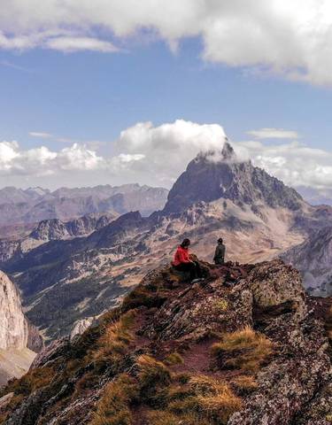 Two people sitting on a rocky peak enjoying mountain views.