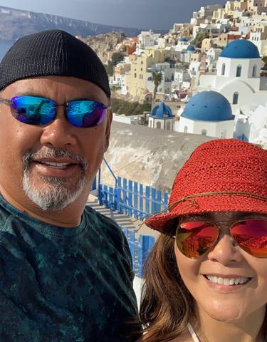 Couple smiling with the iconic blue domes of Santorini in the background.