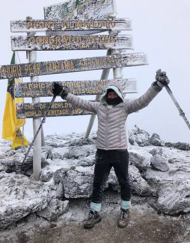 Person celebrating at the snowy summit with a sign displaying the world's highest point.
