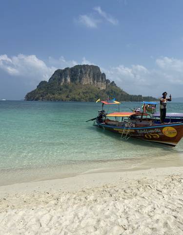 Longtail boats anchored along a tropical beach with clear water.