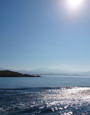 Sailboat cruising through calm waters with islands and mountains in the background.