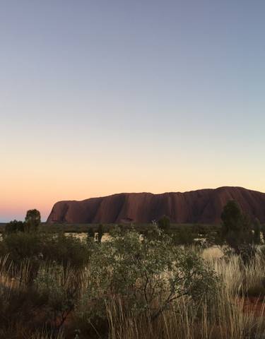 Uluru under a pastel-colored sky at dusk.