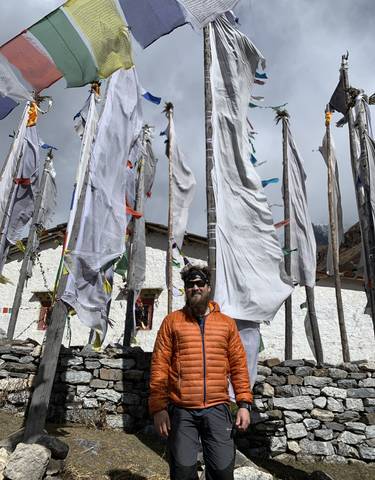 Man in front of prayer flags and mountains.