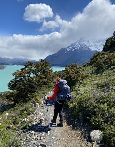 Hiker with backpack walking on a trail by a lake with mountains.