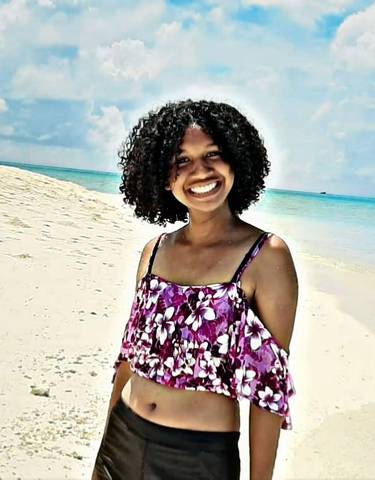 Happy person posing on a white sandy beach with ocean in the background.