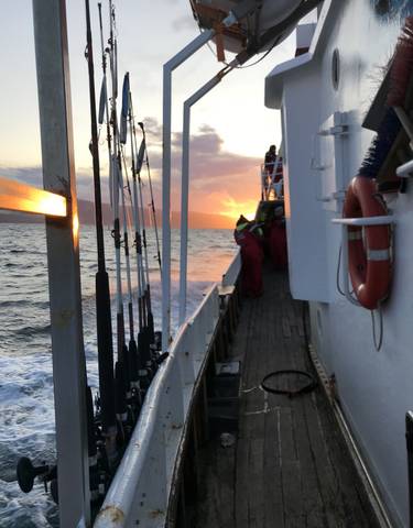 People in red suits on a fishing boat with sunset background.
