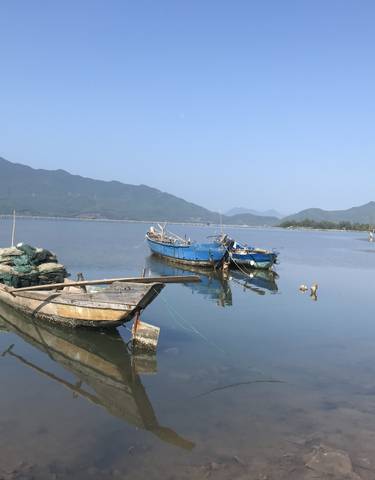 Serene lake with boats and wooden huts, surrounded by mountains.