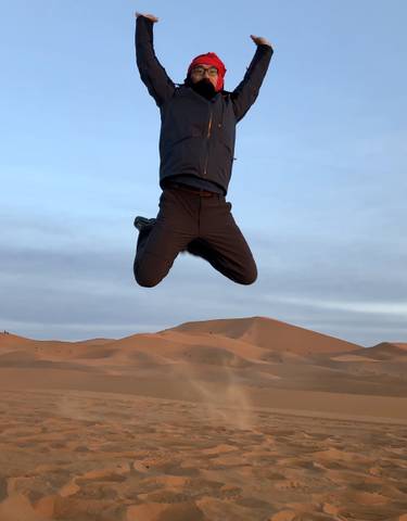 Person jumping in the sand dunes at sunset.