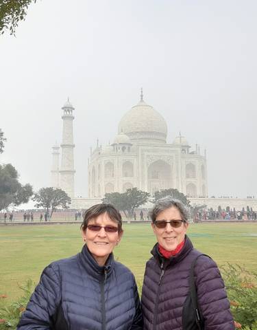 Two women posing in front of the Taj Mahal on a misty day.