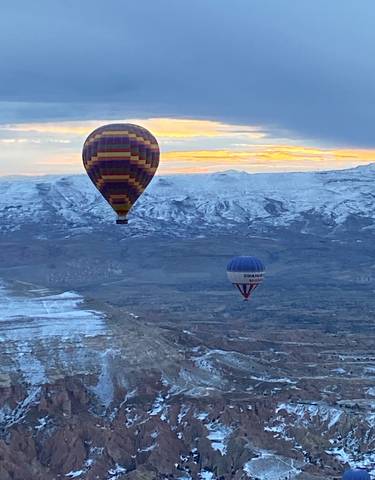 Hot air balloons over snowy Cappadocia landscape.