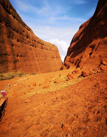 Hikers walking through a canyon with red rock walls.