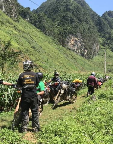 A group of people with motorbikes in a lush, green landscape.