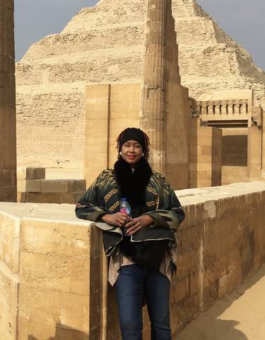 Person sitting by ancient stone structures under a bright sky.