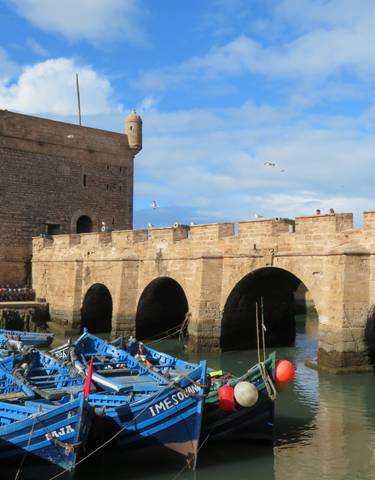 Historic fortified walls with boats floating in a Mediterranean harbor.