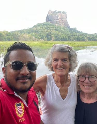 Three people posing in front of a large rock formation and lake