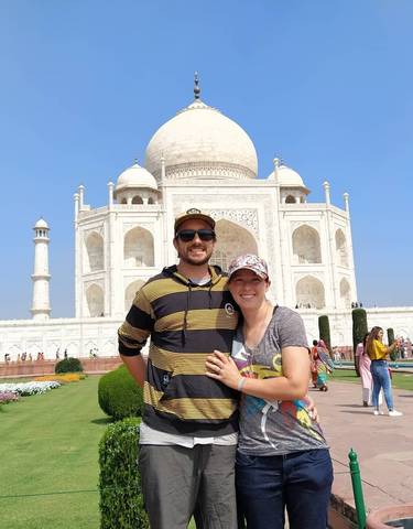 Couple posing in front of the Taj Mahal on a sunny day.