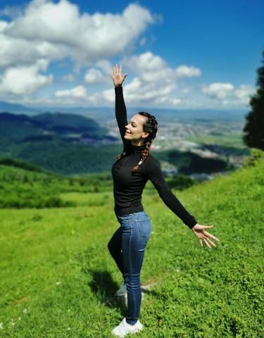 A person joyfully posing with a scenic hilly landscape in the background.
