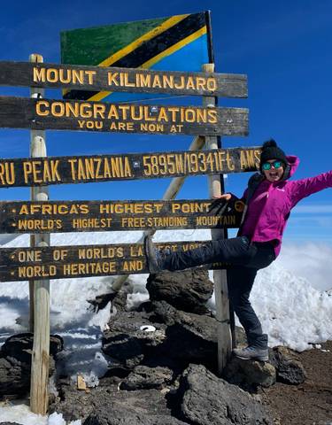 Person celebrating at the sign of Uhuru Peak, Mount Kilimanjaro.