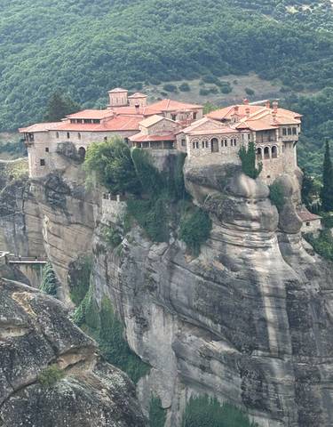 A monastery perched on top of a cliff surrounded by greenery.
