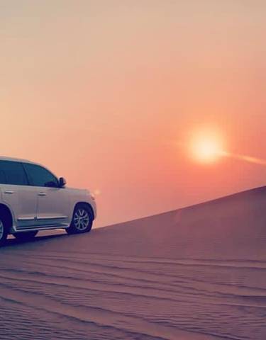 SUV on a sand dune with a sunset in the background