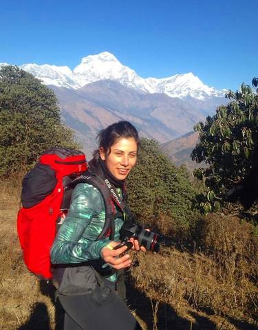 Hiker with backpack and camera posing with mountains in the background.