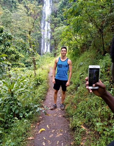 Man standing on a path with a waterfall in the background.