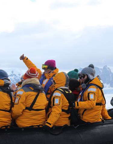 People in yellow jackets on inflatable boats with snowy mountains in the background.