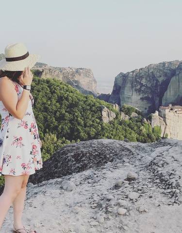 Woman in a floral dress admiring a mountainous landscape with monasteries.