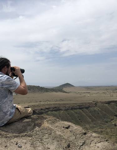 Person photographing a vast open savannah landscape.