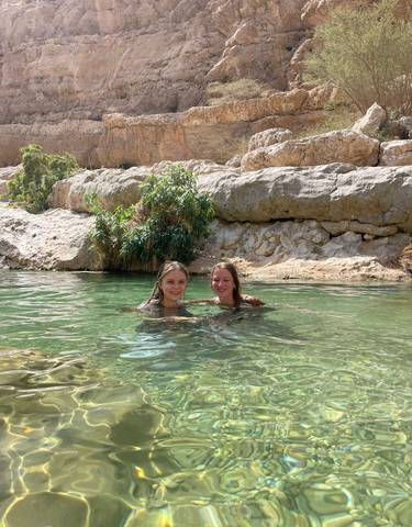 Two women swimming in a natural pool surrounded by rocky terrain.