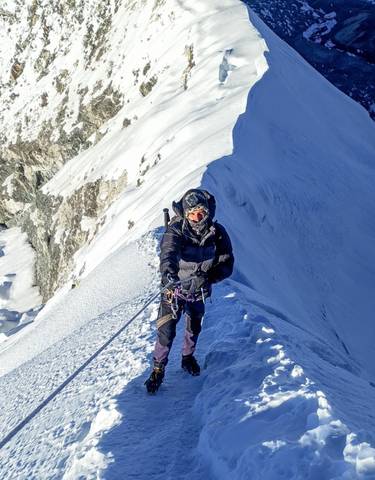 Mountaineer climbing a snowy ridge with safety gear.