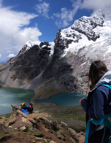 A hiker overlooking a lake and snow-covered mountains.