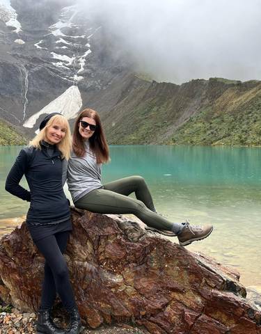Two women relaxing beside a turquoise mountain lake.