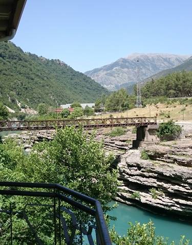 A scenic view of a wooden bridge over turquoise water in a mountainous area.