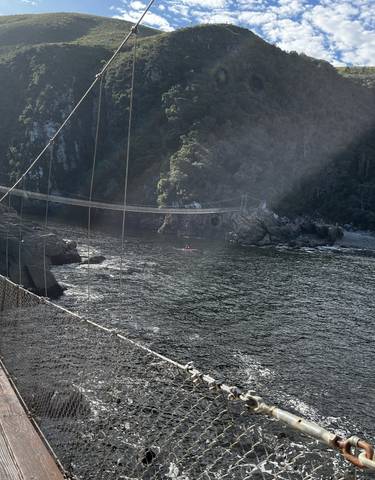 People crossing a rope bridge over a river in the mountains.