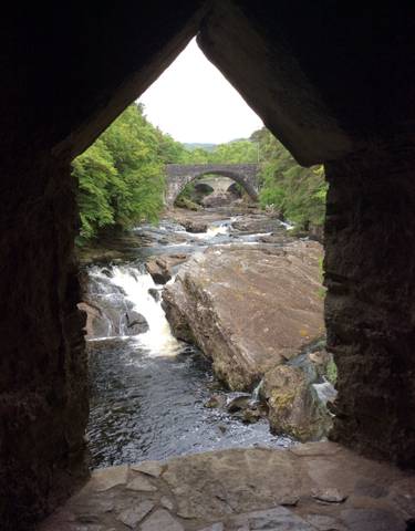 Ancient stone bridge over a river flowing through a forest.