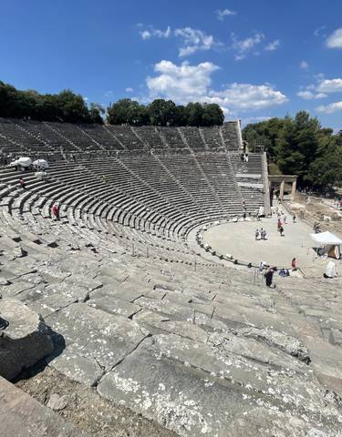 Ancient Greek amphitheater with scattered tourists exploring.