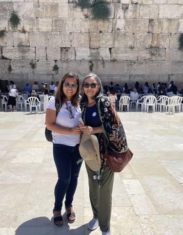 Two women smiling in front of the Western Wall in Jerusalem.