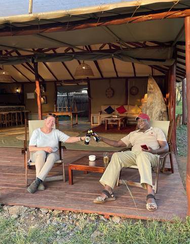 Two people enjoying drinks on a veranda overlooking nature.