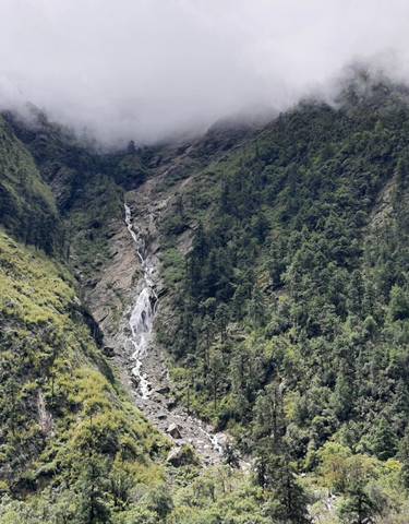 A scenic view of a mist-covered waterfall in a lush mountain landscape.