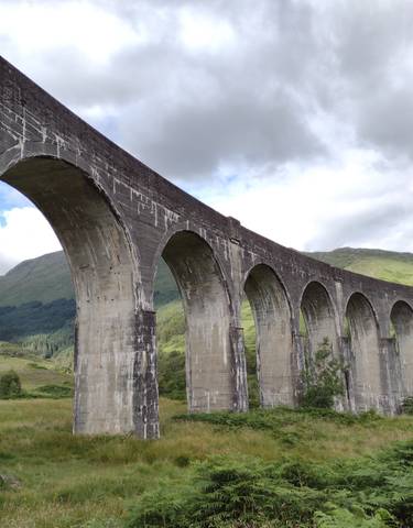 The Glenfinnan Viaduct in Scotland, surrounded by green hills.