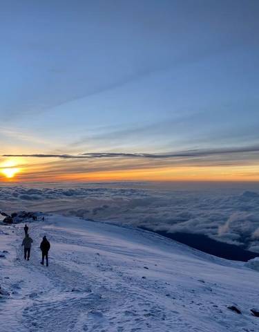 Snowy mountain landscape with two people walking at sunrise.