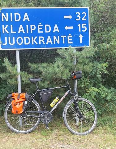 A bicycle parked by a sign pointing to Juodkrante.