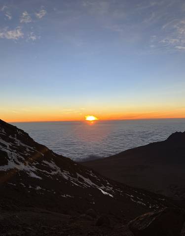 Sunrise over a mountainous landscape with clouds below.