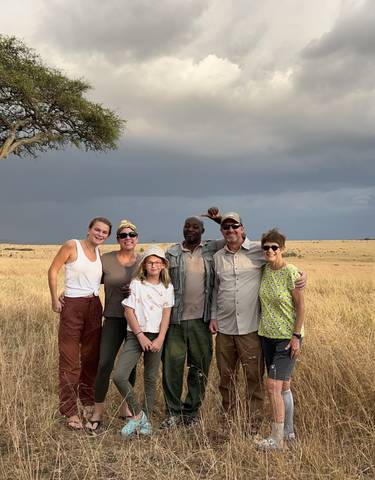 Group of people posing on a savanna with a tree under a cloudy sky.