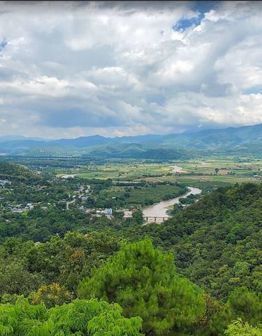 A panoramic view of a valley with a river and mountains in the background.