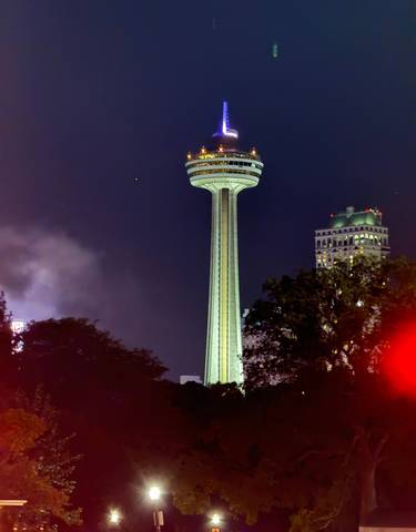 Skylon Tower illuminated at night, surrounded by trees and lights.