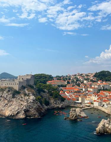 A scenic view of Dubrovnik with medieval walls and orange rooftops along the coastline.