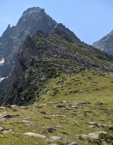 A hiker with a backpack on a grassy ridge with rugged mountains in the background.