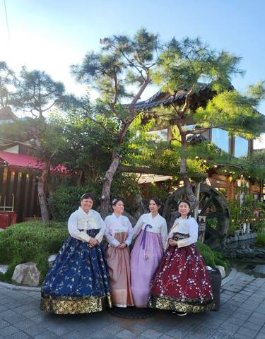Women in traditional Hanbok attire pose in front of a garden.